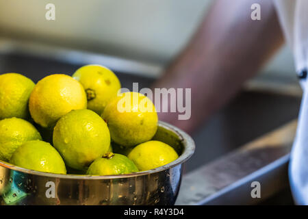 Freshly Washed Limes in the Bowl - Blurred Chef`s Hands in Background Stock Photo